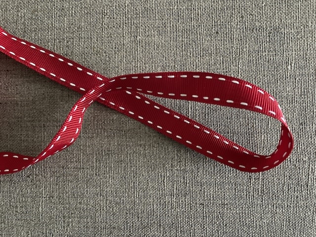 Rød pyntebånd med hvide stikninger. 15 mm bred. Pris pr meter